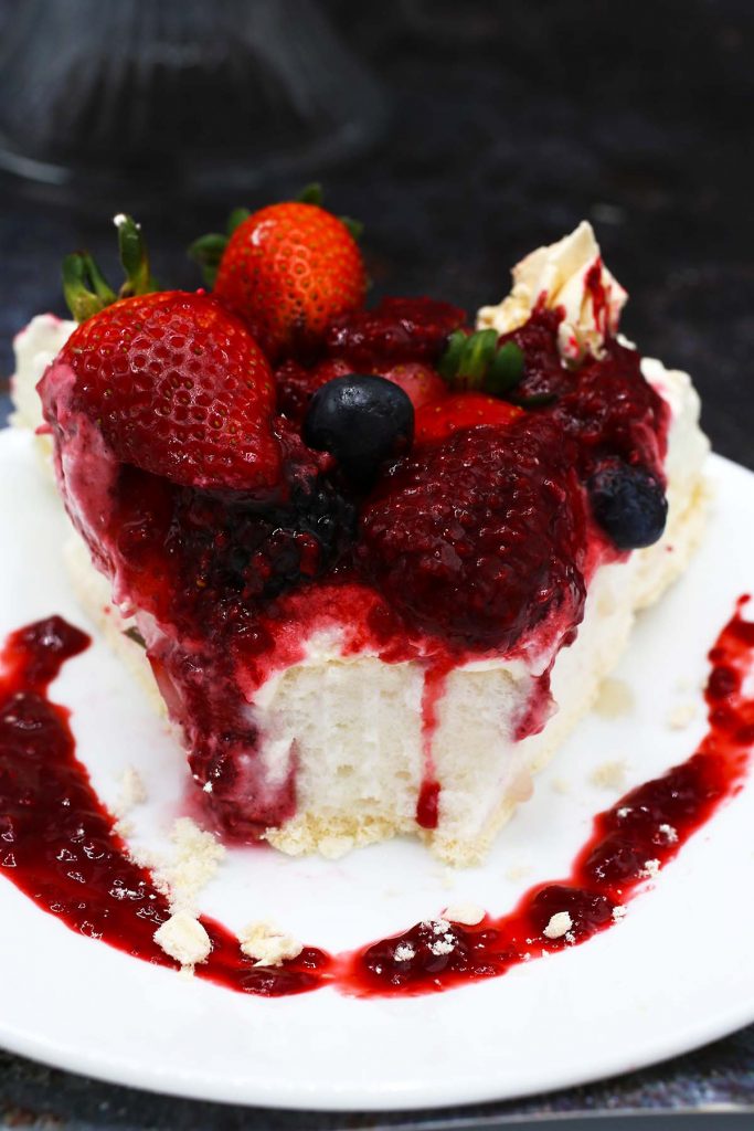 Slice of pavlova on p;ate with fresh raspberry sauce and berries on top.